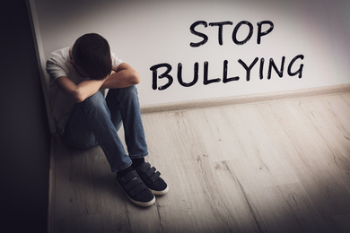 Image of Message STOP BULLYING and upset boy sitting on floor indoors