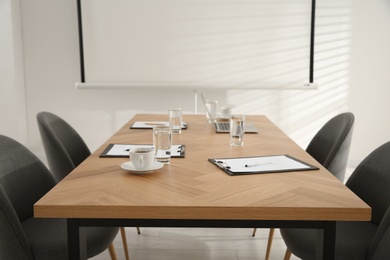 Photo of Conference room interior with glasses of water and clipboards on wooden table