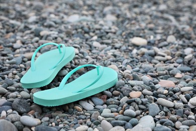 Photo of Stylish turquoise flip flops on pebble seashore. Space for text