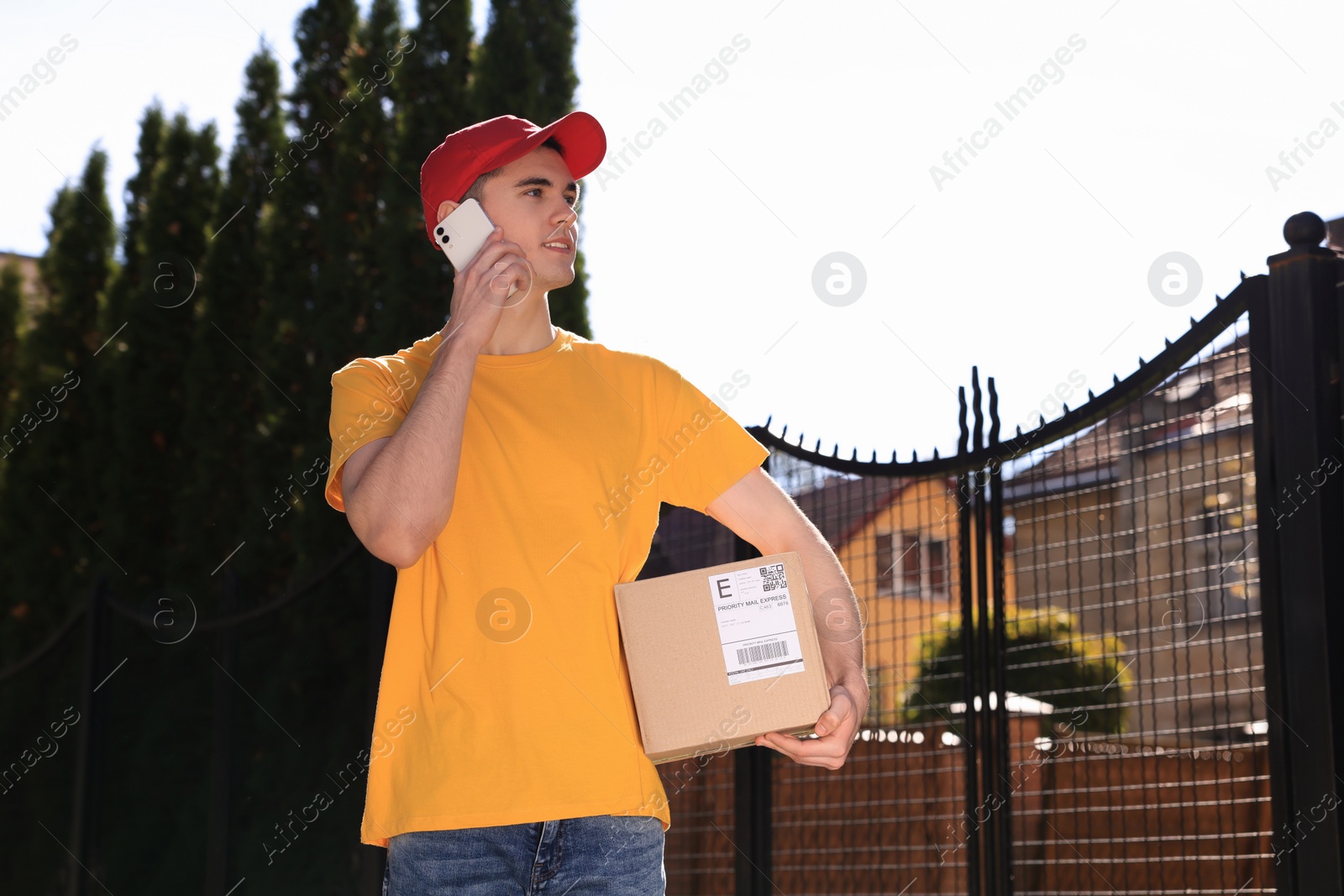 Photo of Courier with parcel talking by smartphone on city street