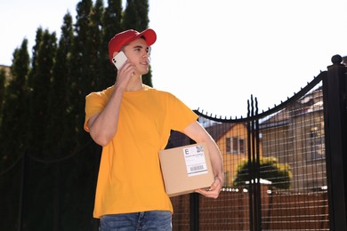 Courier with parcel talking by smartphone on city street