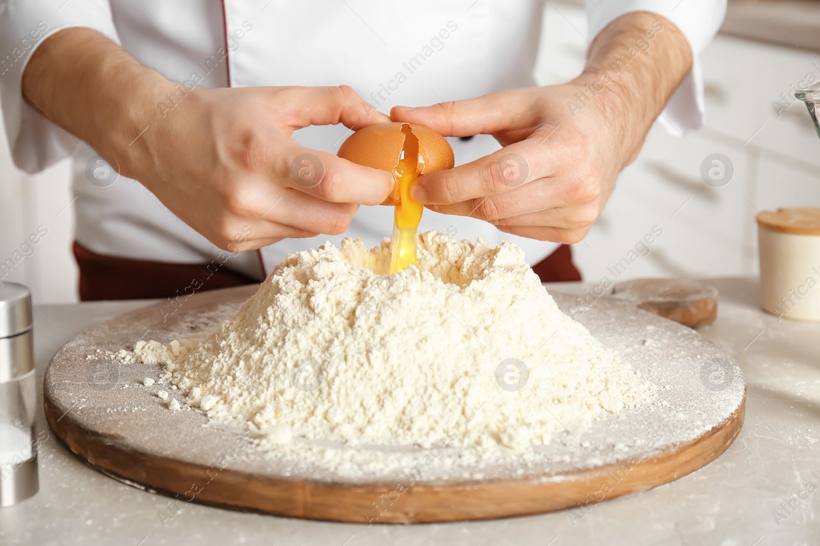 Photo of Male chef breaking egg over pile of flour on board in kitchen