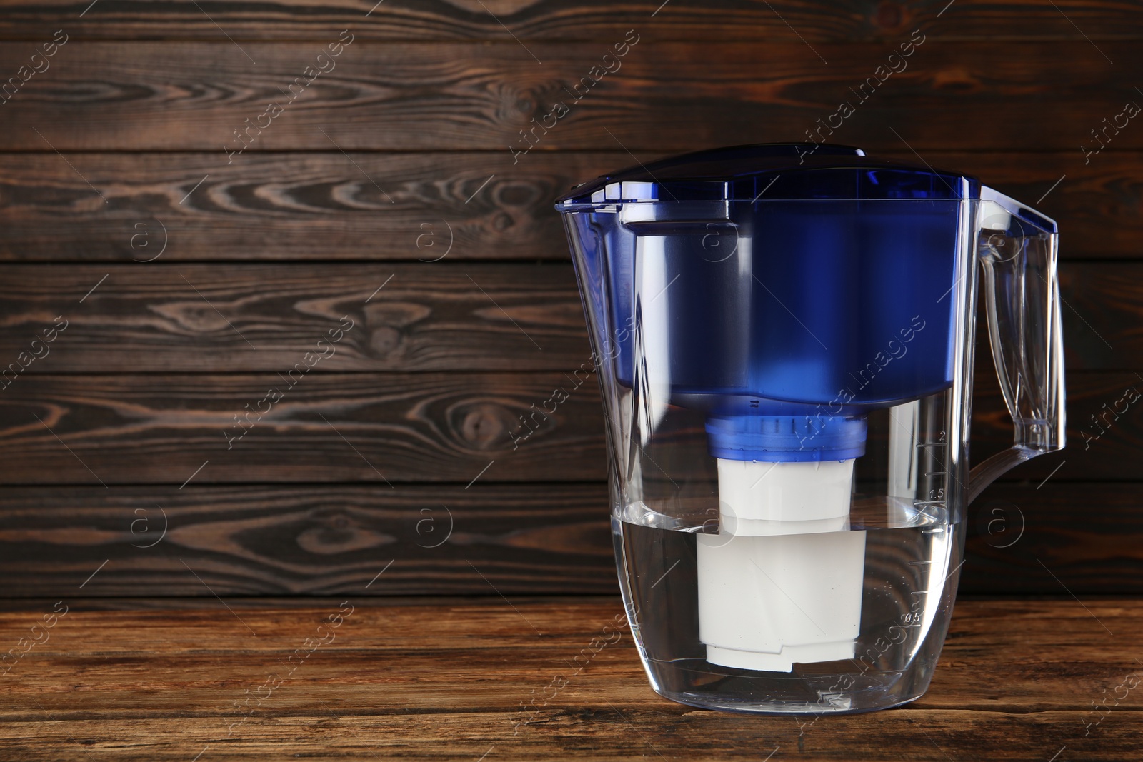 Photo of Filter jug with purified water on wooden table. Space for text