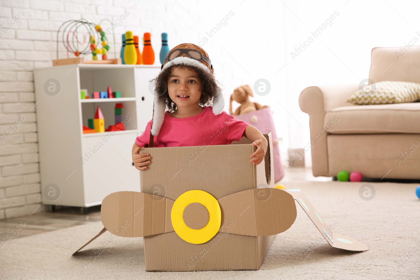 Photo of Cute African American child playing with cardboard plane at home