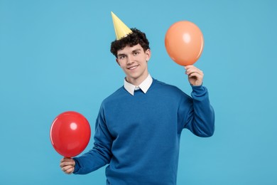 Young man in party hat with balloons on light blue background