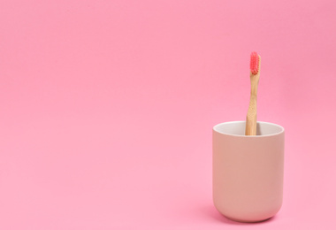 Photo of Toothbrush made of bamboo in holder on pink background. Space for text