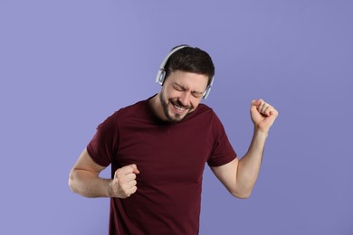 Photo of Happy man in headphones enjoying music and dancing on purple background