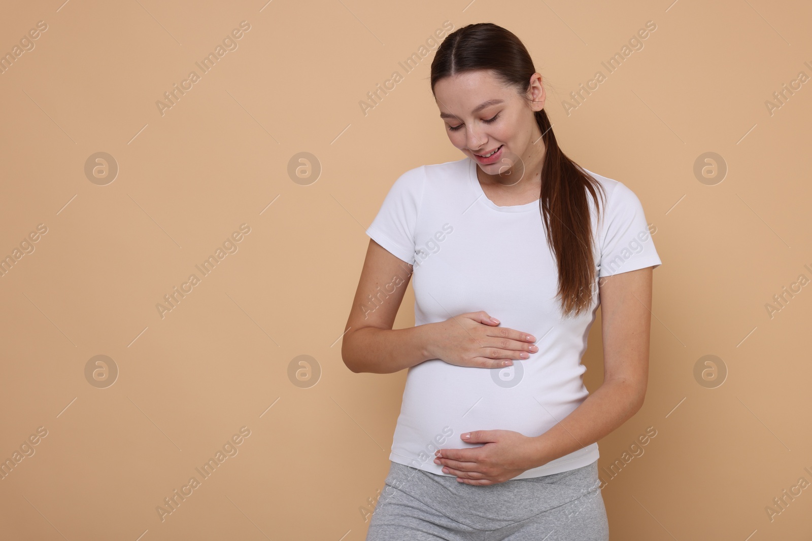 Photo of Beautiful pregnant woman in white T-shirt on beige background, space for text