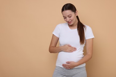 Beautiful pregnant woman in white T-shirt on beige background, space for text