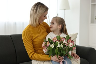 Photo of Little daughter congratulating her mom with Mother`s Day at home. Woman holding bouquet of alstroemeria flowers