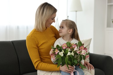 Little daughter congratulating her mom with Mother`s Day at home. Woman holding bouquet of alstroemeria flowers