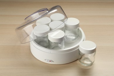 Modern yogurt maker with empty jars on wooden table