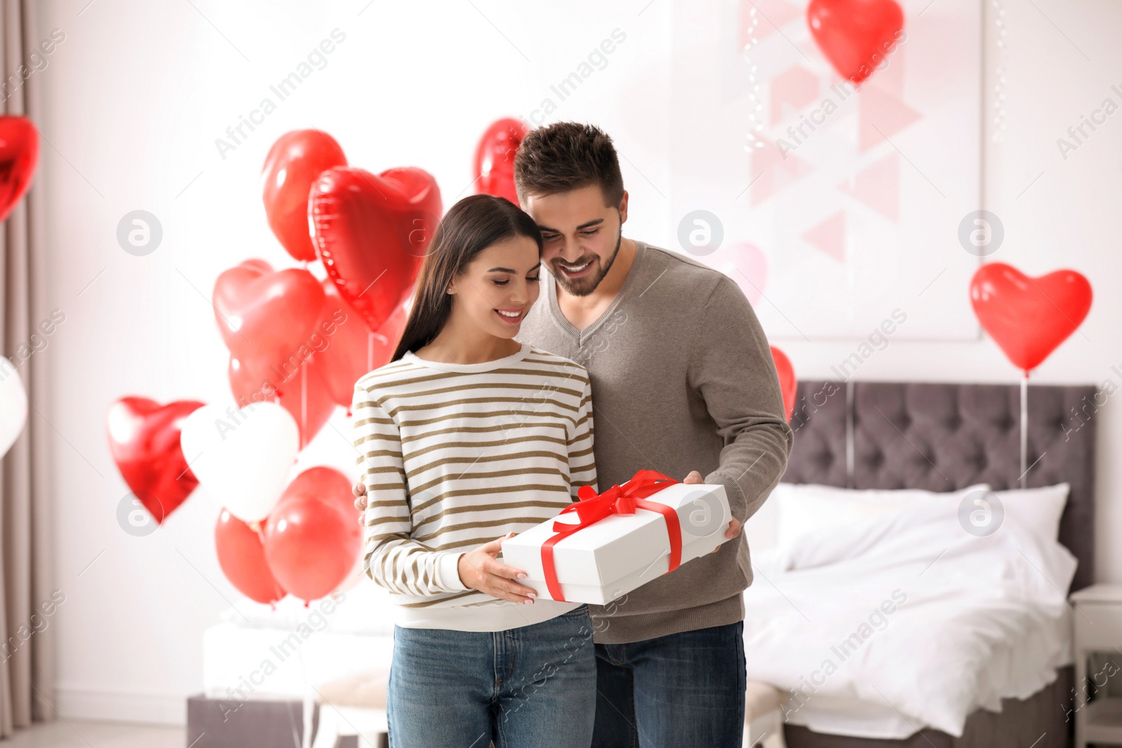 Photo of Happy young couple in bedroom decorated with heart shaped balloons. Valentine's day celebration