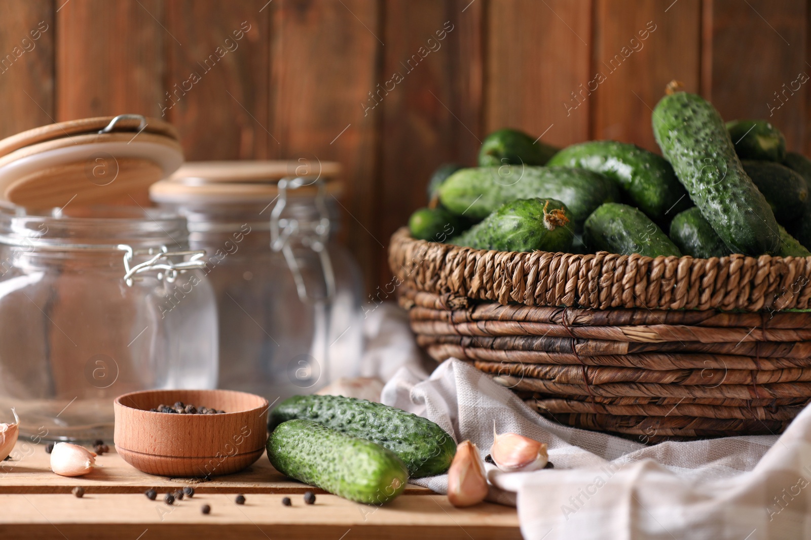 Photo of Fresh cucumbers and other ingredients near empty jars prepared for canning on wooden table