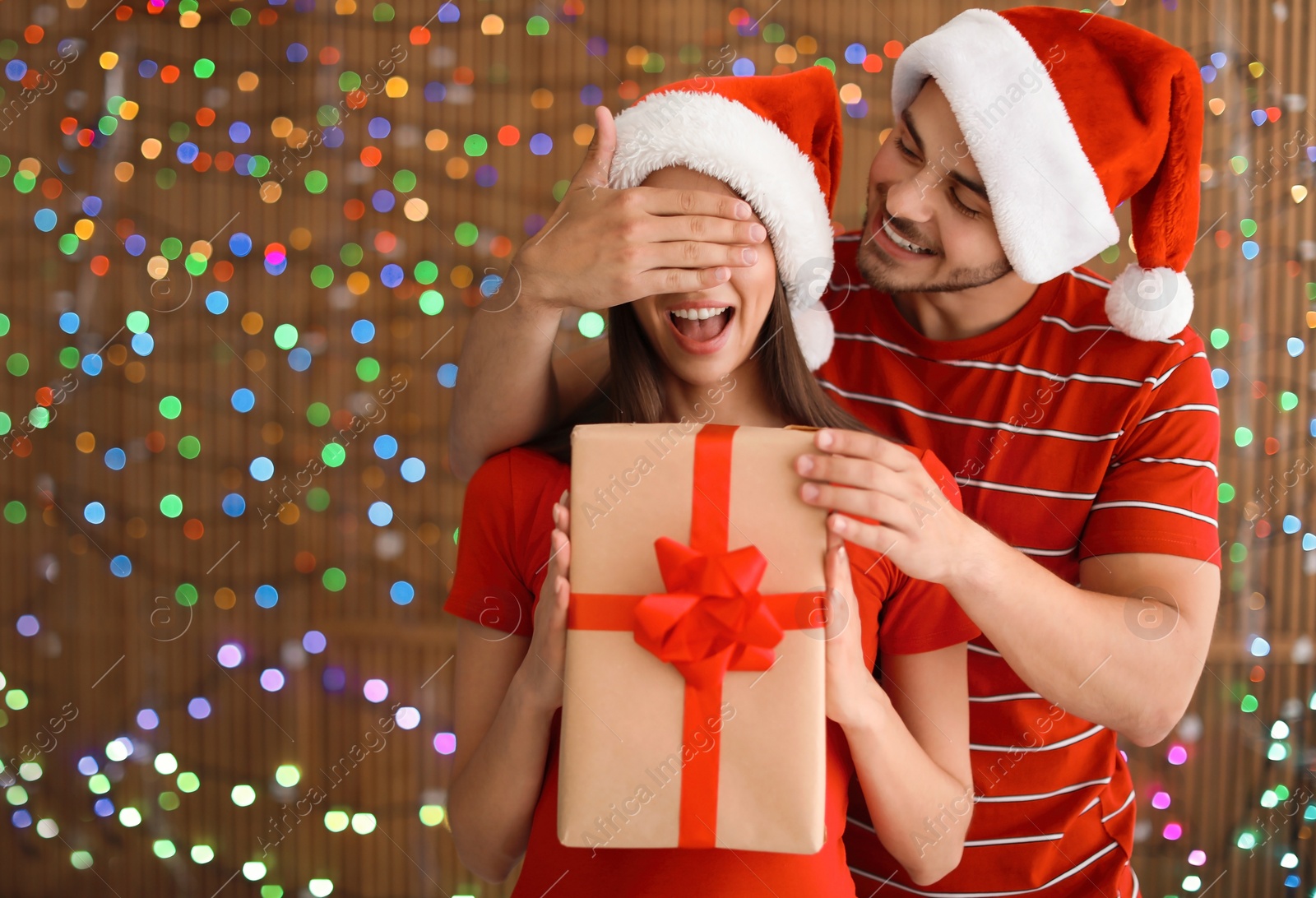 Photo of Young couple in Santa hats with Christmas gift on blurred lights background