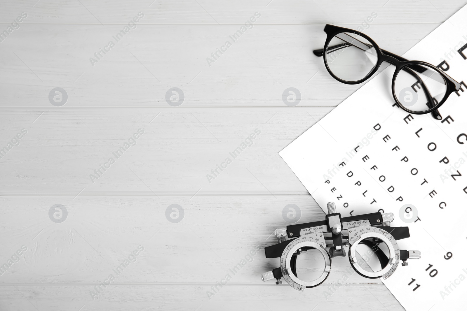 Photo of Trial frame, eye chart test, glasses and space for text on white wooden table. Ophthalmologist tools