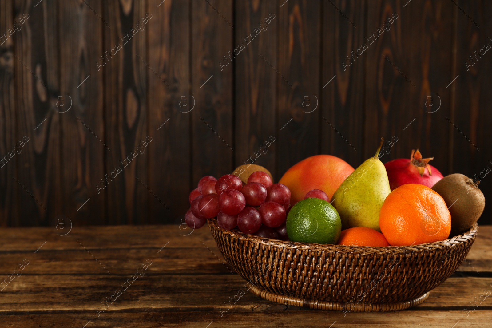 Photo of Fresh ripe fruits in wicker bowl on wooden table, space for text