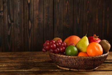 Photo of Fresh ripe fruits in wicker bowl on wooden table, space for text