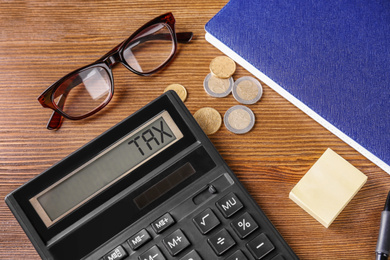 Calculator with word Tax, glasses, coins and notebook on table