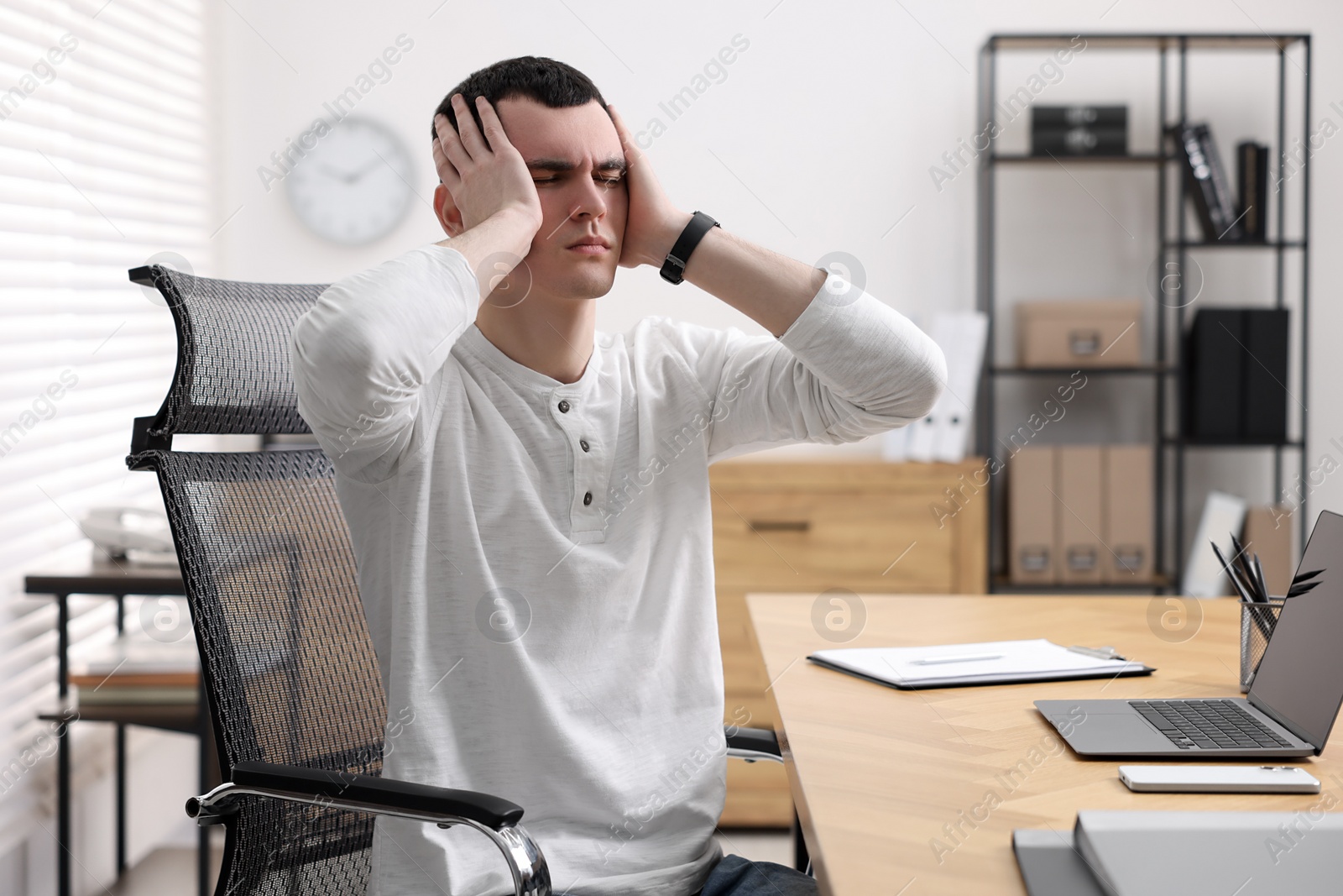 Photo of Young man suffering from headache at workplace in office