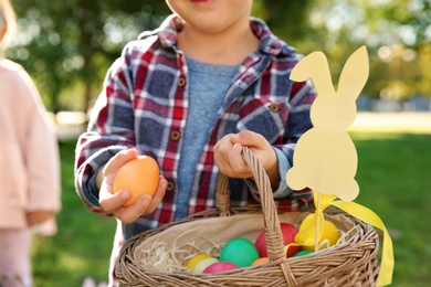 Photo of Little child with basket of Easter eggs in park, closeup