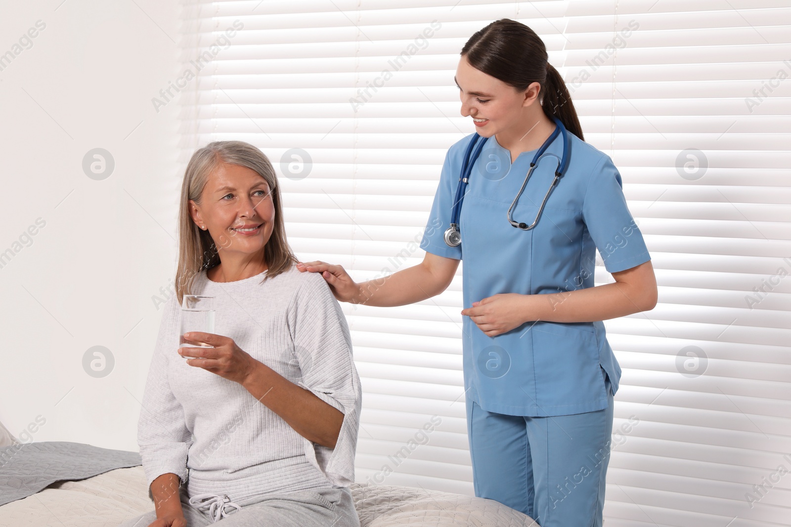 Photo of Senior woman with glass of water and young healthcare worker indoors