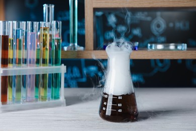 Laboratory flask and test tubes with colorful liquids on white wooden table. Chemical reaction