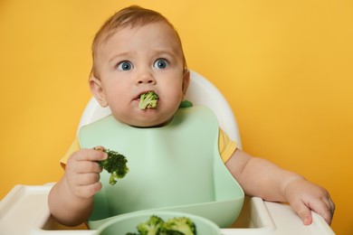 Photo of Cute little baby wearing bib while eating on yellow background