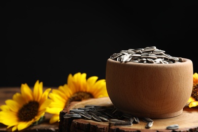 Photo of Raw sunflower seeds on wooden stand against black background. Space for text