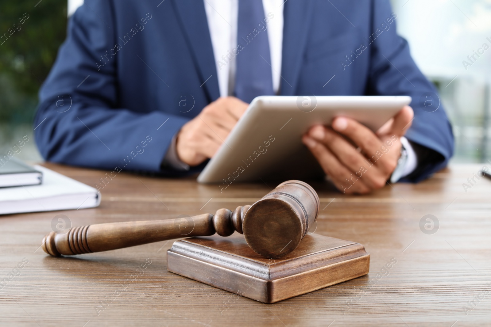 Photo of Wooden gavel and blurred lawyer with tablet on background