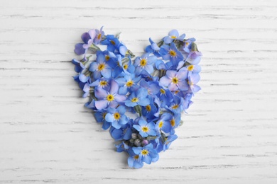 Photo of Heart made of amazing spring forget-me-not flowers on white wooden background, top view