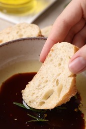 Woman dipping piece of bread into balsamic vinegar with oil and rosemary in bowl closeup