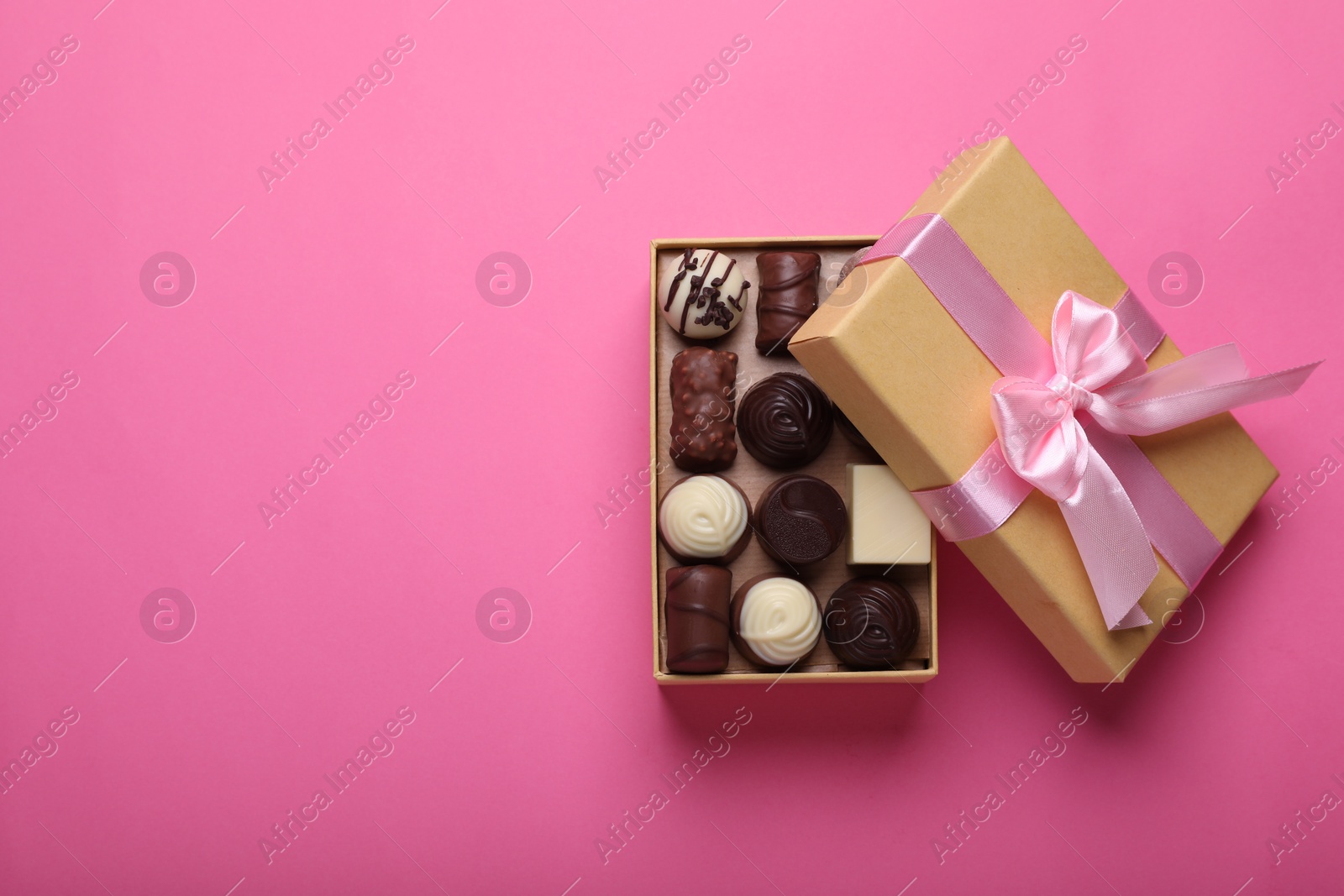 Open box with delicious chocolate candies on pink background, top view. Space for text Photo of Open box with delicious chocolate candies on pink background, top view. Space for text