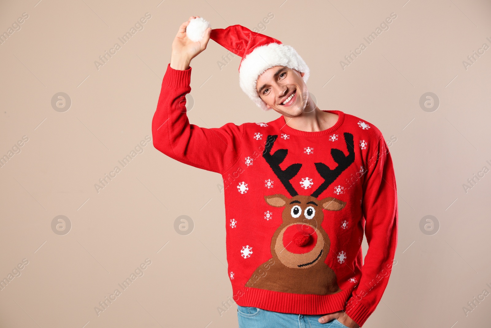 Photo of Portrait of young man in Christmas sweater and Santa hat on beige background