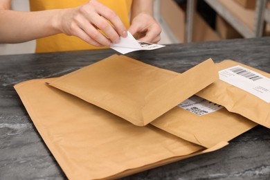 Photo of Post office worker sticking barcode on parcel at counter indoors, closeup