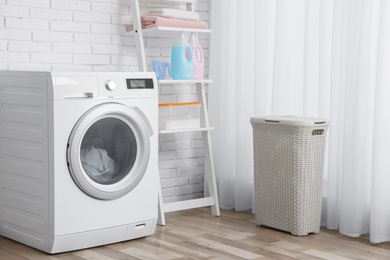Photo of Modern washing machine near brick wall in laundry room interior