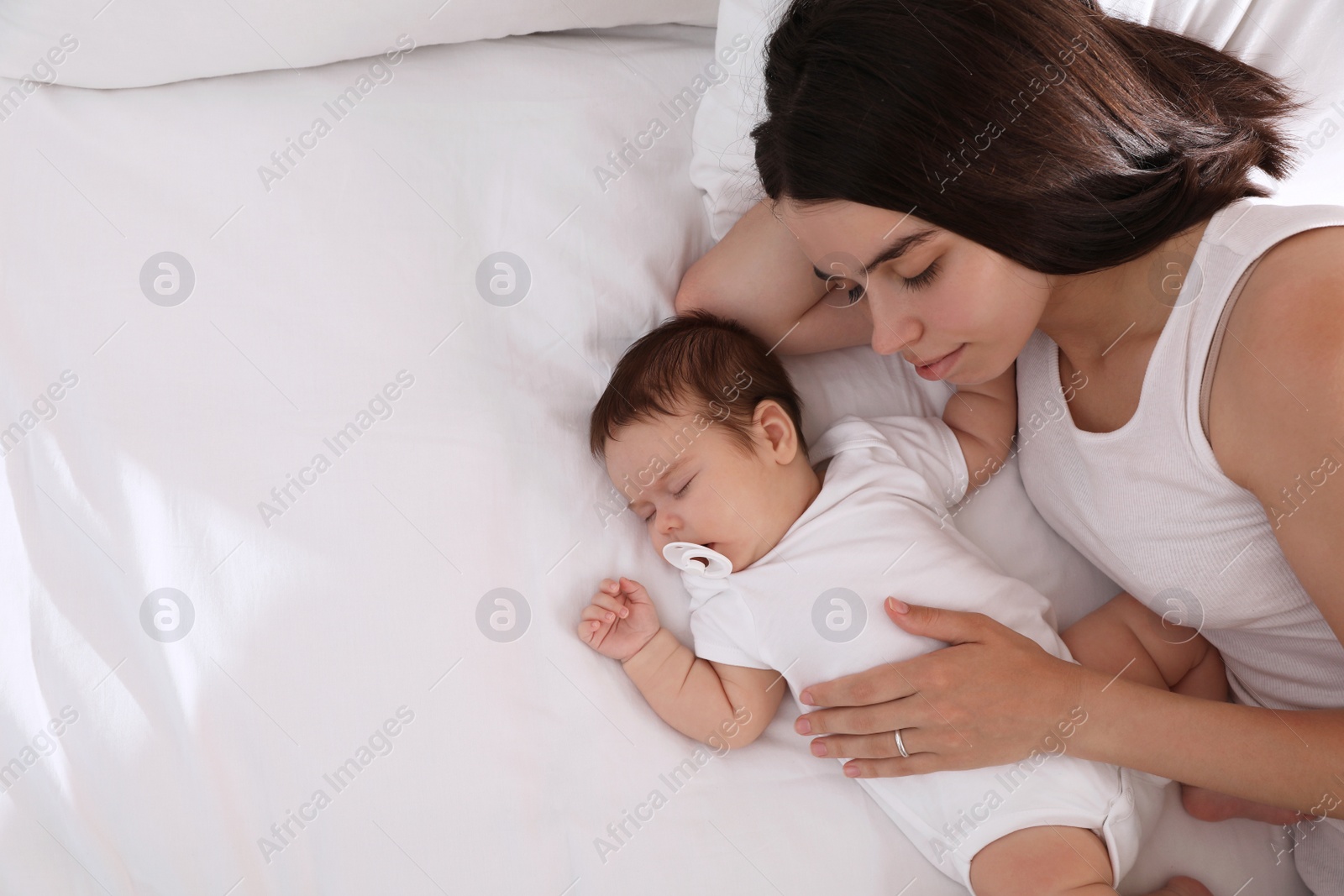 Photo of Young mother resting near her sleeping baby on bed, top view. Space for text