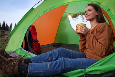 Young woman with cup of drink in camping tent outdoors