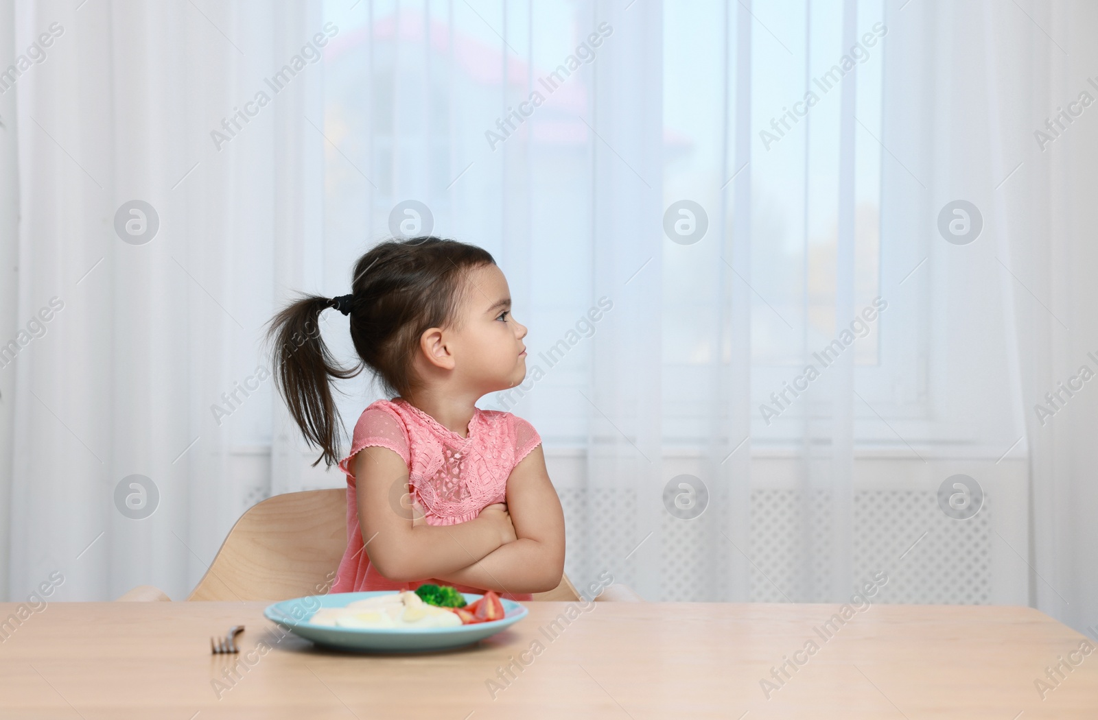 Photo of Cute little girl refusing to eat her breakfast at home, space for text