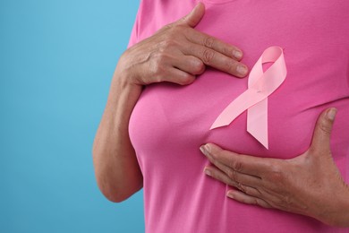 Woman with pink ribbon on light blue background, closeup and space for text. Breast cancer awareness