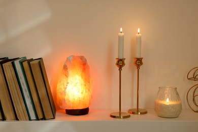 Photo of Pair of beautiful candlesticks, scented candle and salt lamp on white shelf
