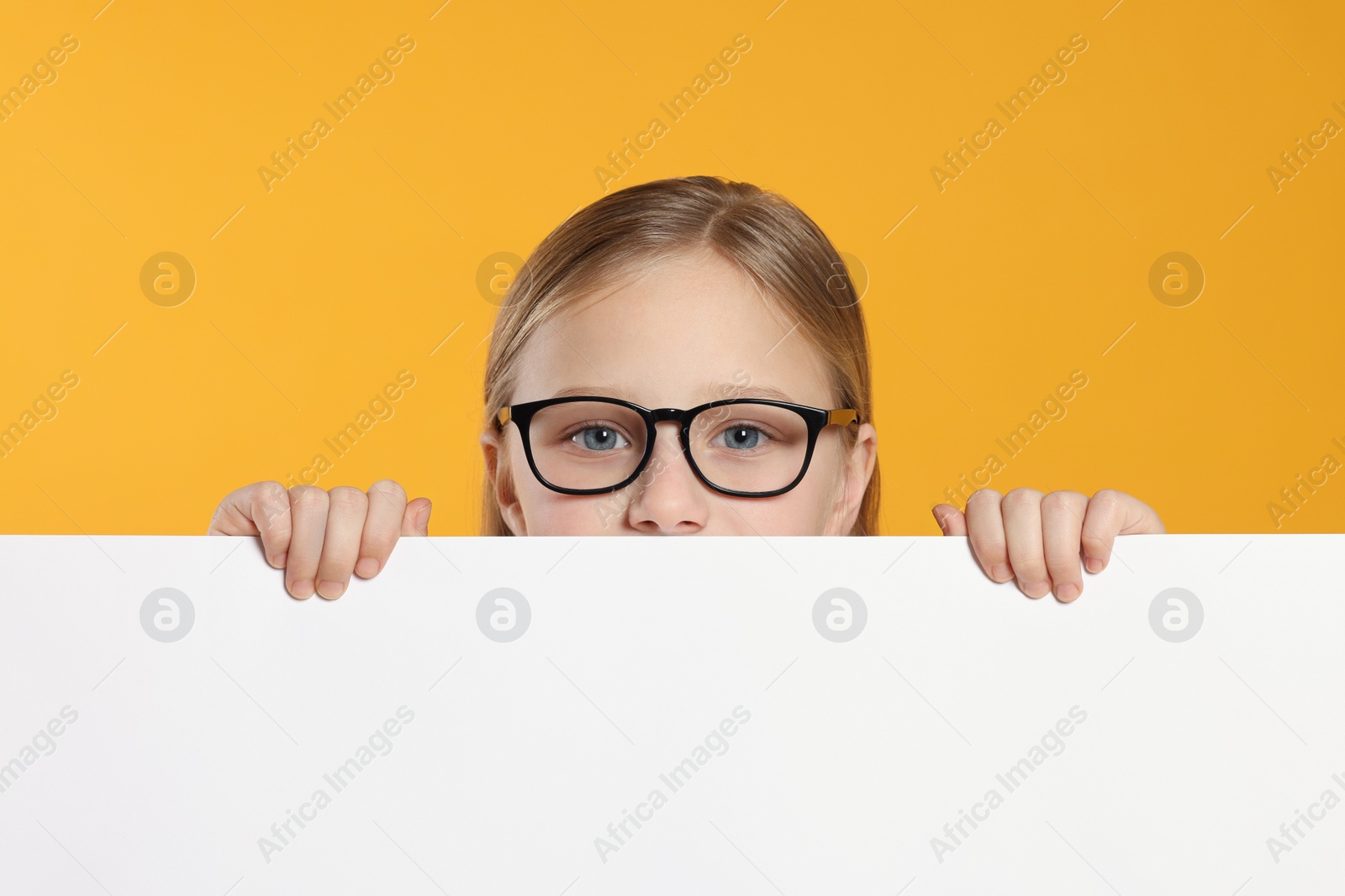 Photo of Cute girl looking out of placard against orange background. Space for text