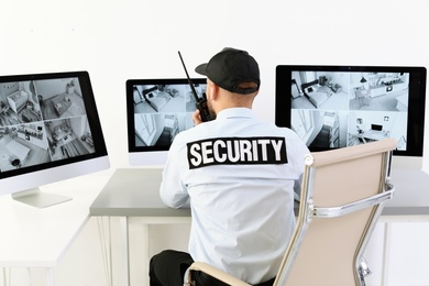 Photo of Male security guard with portable transmitter monitoring home cameras indoors