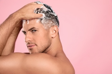 Photo of Handsome man washing hair on pink background. Space for text