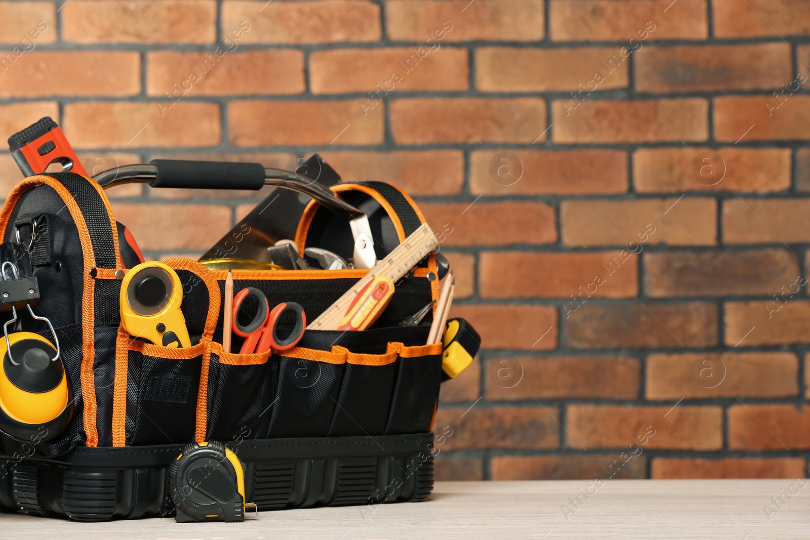 Photo of Bag with different tools for repair on white wooden table near brick wall. Space for text