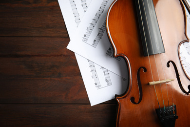 Photo of Beautiful violin and note sheets on wooden table, flat lay. Space for text