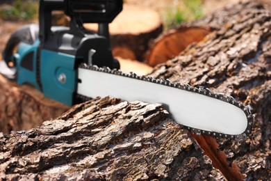 Photo of Modern electric saw and wooden log outdoors