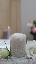 Glass with bath salt and beautiful flowers on wicker mat in bathroom