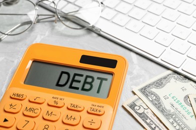 Calculator with word Debt, money and keyboard on light grey marble table, closeup