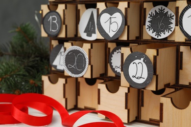 Photo of Wooden advent calendar and red ribbon on white table, closeup